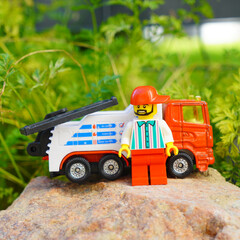 Obraz premium Lego tow truck toy with a Lego figure standing on a rock in a garden setting