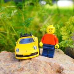 Obraz premium Lego figure stands next to a yellow toy sports car on a rock