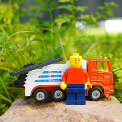 Obraz premium Lego figure stands proudly next to a toy tow truck on a rock