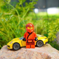 Obraz premium Lego Ninjago figure stands with a yellow sports car on a rock