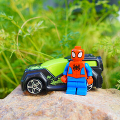 Obraz premium Spider-Man toy figure stands next to a toy car on a rock