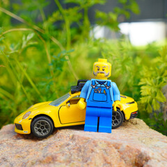 Obraz premium Lego figure with yellow sports car on a rock in front of green foliage