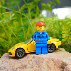 Obraz premium lego figure with yellow sports car on a rock with green foliage background