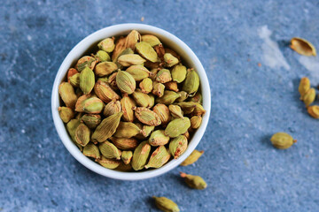 Green cardamom seeds in a bowl on a blue background