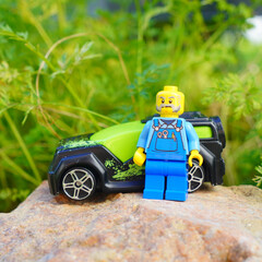 Naklejka premium Lego mechanic figure stands next to a toy car on a rock in a garden