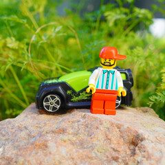 Naklejka premium Lego minifigure stands next to a toy car on a rock in a natural setting