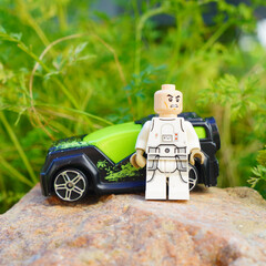 Naklejka premium Lego minifigure stands beside a toy car on a natural rock surface