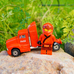 Naklejka premium Lego Ninjago figure stands next to a red Coca-Cola semi-truck toy on a rock
