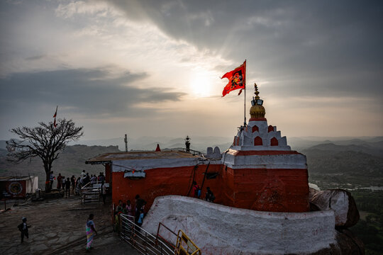Hampi, India - 02 November 2025: View of the vibrant red and white Hanuman Temple atop a rocky hill, its flag fluttering against the backdrop of a clouded sky.