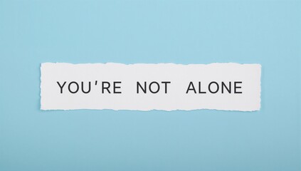 Torn white sticky note on blue background with message YOU'RE NOT ALONE, theme of encouragement during tough times