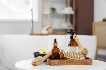 Tray with different massage brushes, sea salt, flower and cosmetic products on table in bathroom