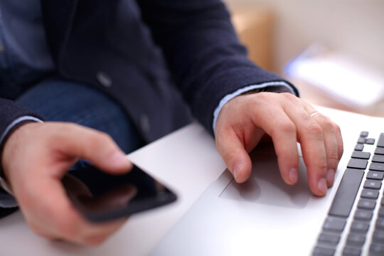 Businessman at his workplace uses a smartphone and laptop - Powered by Adobe