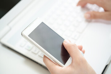 person holding smartphone while using laptop keyboard