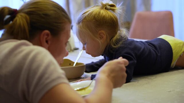 Young child's determined mealtime adventure at home, eagerly learning to spoon-feed from bowl.