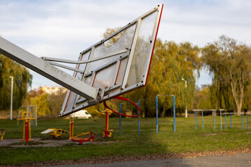 A broken and lopsided basketball hoop stands on an open-air sports court