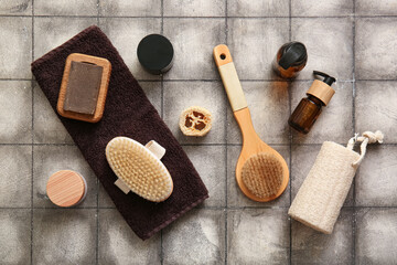Massage brushes with soap, cosmetic products and towel on grey tile background