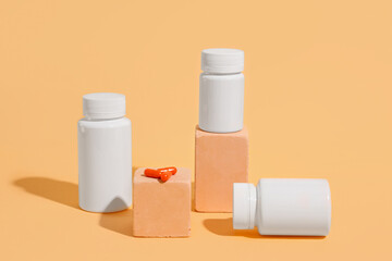 Decorative podiums with blank plastic vitamin bottles and pills on orange background