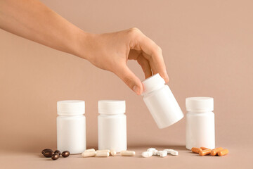 Female hand with blank plastic vitamin bottles and different pills on brown background