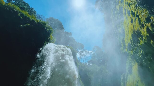 Blawan Waterfall around the Kawa Ijen Crater, hidden in the tropical jungle, East Java, Indonesia. A picturesque view of a powerful waterfall surrounded by sharp rocks covered with moss and plants. 4К