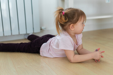 Fototapeta premium Child lying on the wooden floor and resting near the radiator. Peaceful moment of childhood calmness, observation, and quiet time at home.