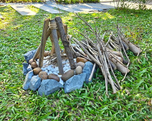 A small artificial bonfire is placed in the garden to decorate place. Large grey and brown rocks are arranged in circle around small white rocks. Small pine logs are used to arrange them like bonfire.
