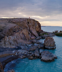 A lonely traveler on the edge of a rocky cliff, contemplating the endless turquoise waters of Lake Balkhash at sunset. The greatness of the nature of Kazakhstan.
