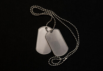 Blank metal military dog tags on silver chain isolated on black surface