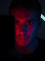 Intense young man illuminated by striking red and blue neon lights, conveying deep thought and modern mystery, perfect for tech or creative projects.