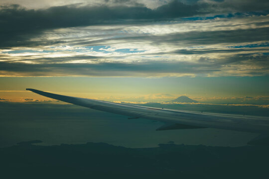 View of Mount Fuji from airplane window at sunset with wing and clouds