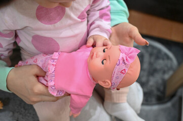 A baby is holding a doll. Mom and child. A mother holds a child in her arms. A child and a toy.