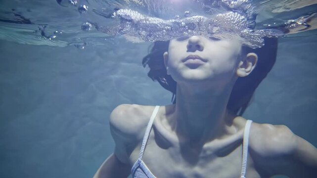 Underwater video close-up of a serene girl with closed eyes, captured from a frontal angle, highlighting tranquility and fluidity in a dreamy style.