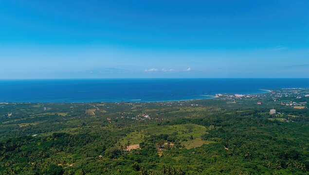 Aerial perspective of a vibrant green landscape, seaside village, and vast blue ocean beneath a clear sky, emphasizing the tranquility of nature