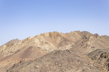 anoramic view of barren, multi-hued desert mountains under a clear sky