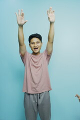Cheerful young man raising his hands in celebration against a vibrant teal background, radiating positivity and youthful energy, perfect for lifestyle ads