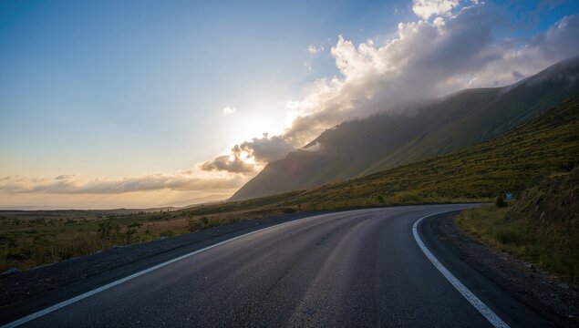 Asphalt road bordered by green mountain and cloudy sky at sunrise, erosion risk