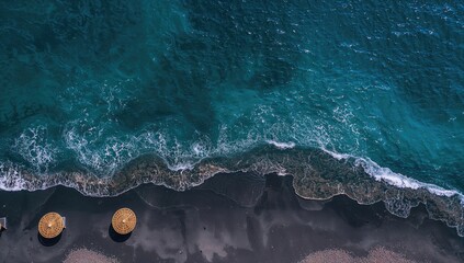 Fototapeta premium Aerial view of black sand beach with turquoise waters and straw umbrellas, ideal for vacation travel