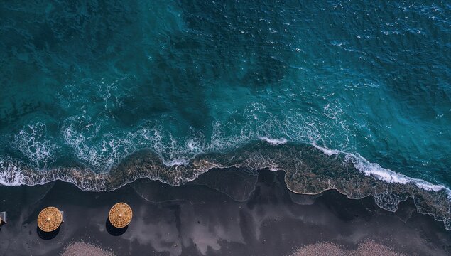 Aerial view of black sand beach with turquoise waters and straw umbrellas, ideal for vacation travel - Powered by Adobe