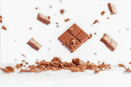 Chocolate squares are suspended mid-air, with crumbs scattered below, showcasing a dynamic food styling technique in bright lighting