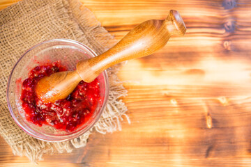 Fresh cranberries mashed in glass bowl with wooden pestle. Homemade organic cranberry puree, rustic healthy food concept, natural vitamins and traditional autumn recipe.