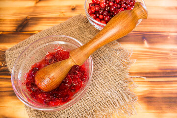 Fresh cranberries mashed in glass bowl with wooden pestle. Homemade organic cranberry puree, rustic healthy food concept, natural vitamins and traditional autumn recipe.