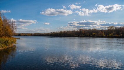 Fototapeta premium Uz River during autumn, reflecting trees and clouds in shallow water, highlighting urban density