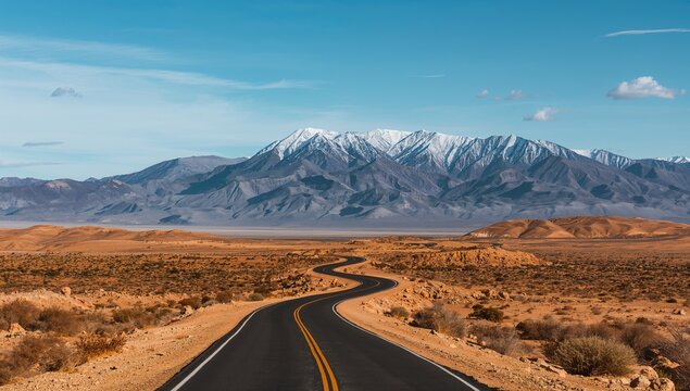 A winding road traversing arid desert landscapes, framed by towering snow-covered mountains, seasonal change - Powered by Adobe