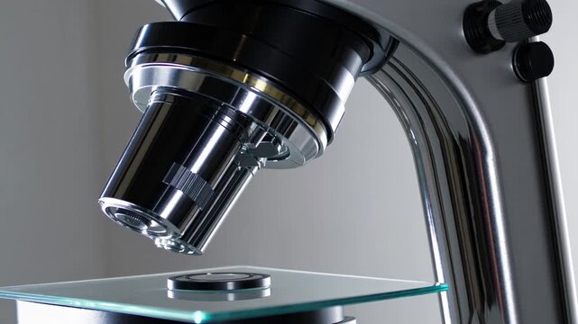 Close-up video of a microscope lens at a low angle, highlighting the sleek, metallic design and scientific focus, emphasizing precision and detail.