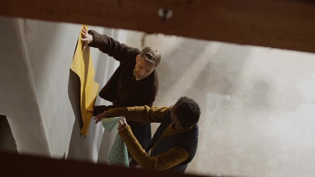 From above shot of Black male interior designer showing wallpaper samples to Caucasian client at renovation site, collaborating on home remodeling ideas and aesthetic design planning