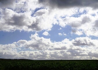 Himmellandschaft mit blauem Himmel mit weißem Wolkengebilde und Licht hinter grünem Ackerfeld bei Sonne, Sturm und Regen am Nachmittag im Herbst