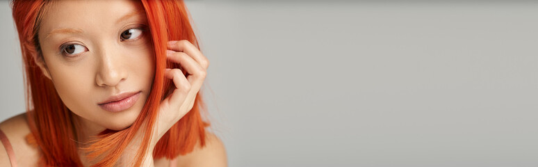 Stunning young woman with bright red hair poses gracefully against a soft grey backdrop