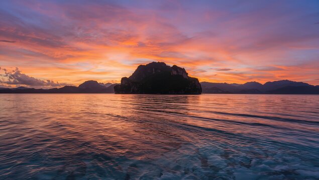 A picturesque island embraced by clear waters, witnessing a vibrant sunset casting silhouettes, seasonal change