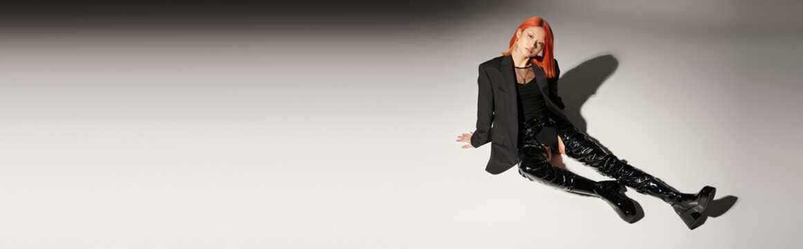 full length of sassy asian woman in sexy latex boots and blazer sitting on grey backdrop, banner