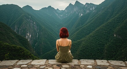 Woman sitting on stone wall overlooking vast green mountain landscape.