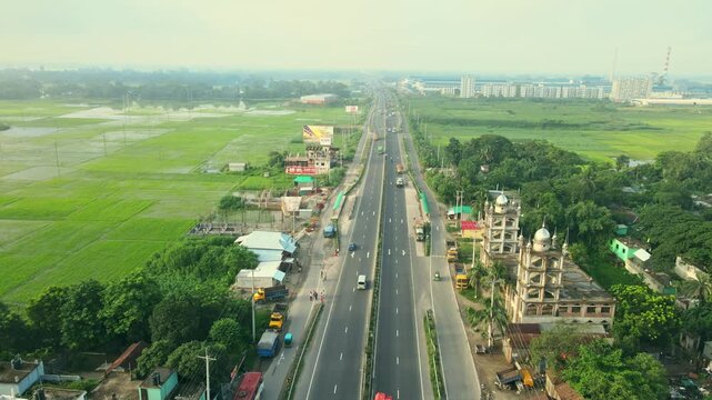 Aerial view of a long highway cutting through lush green vegetation and agricultural fields, Tangail, Rajshahi Division, Bangladesh.